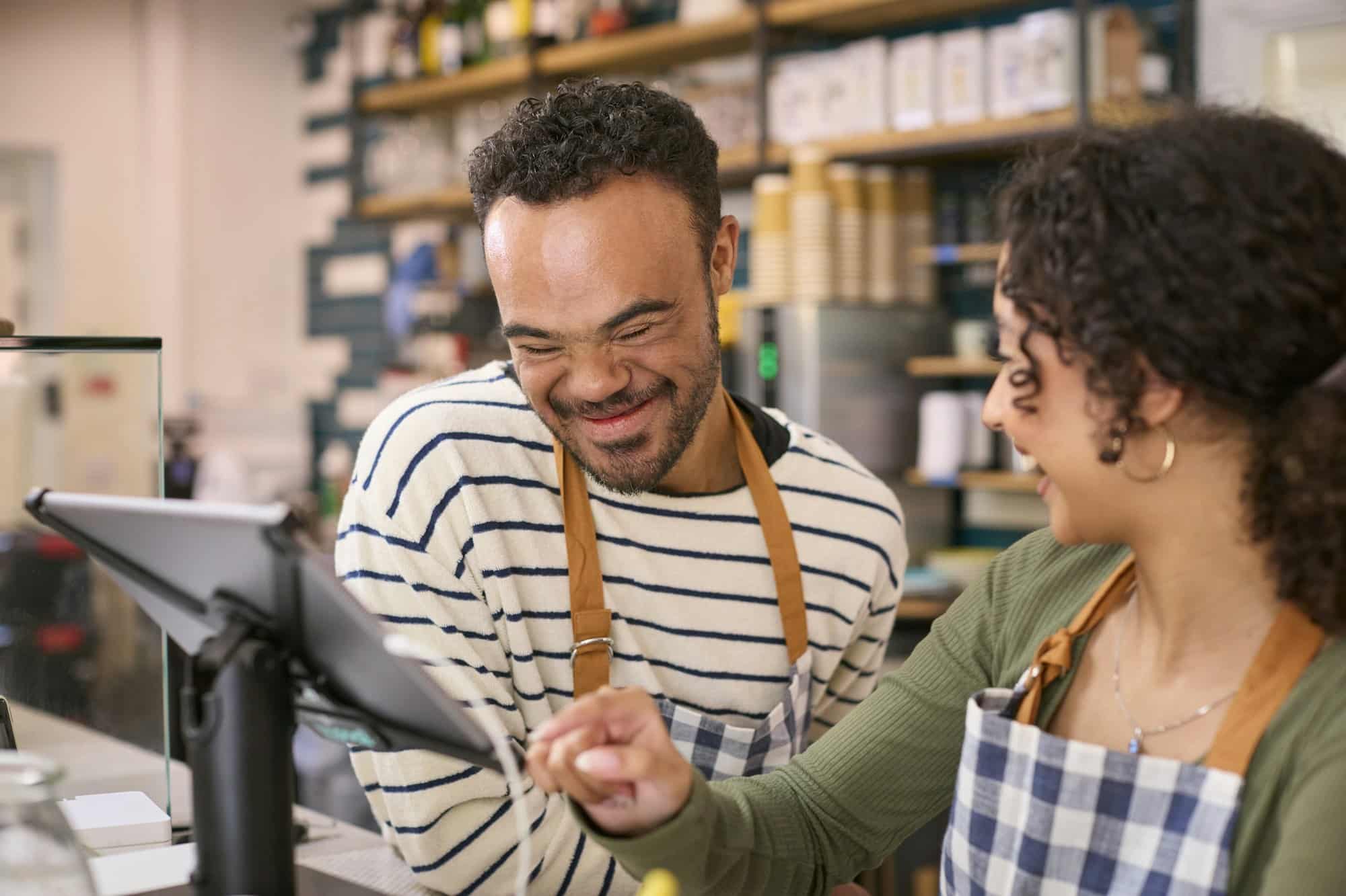 Woman Working In Food Shop Training Man With Down Syndrome How To Use Checkout